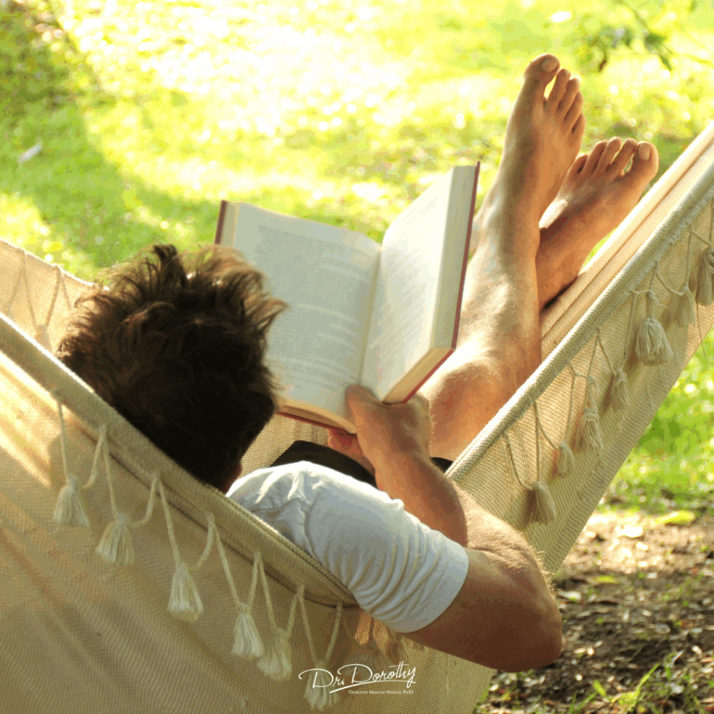 man getting some rest while relaxing on a hammock reading a book on a sunny summer afternoon