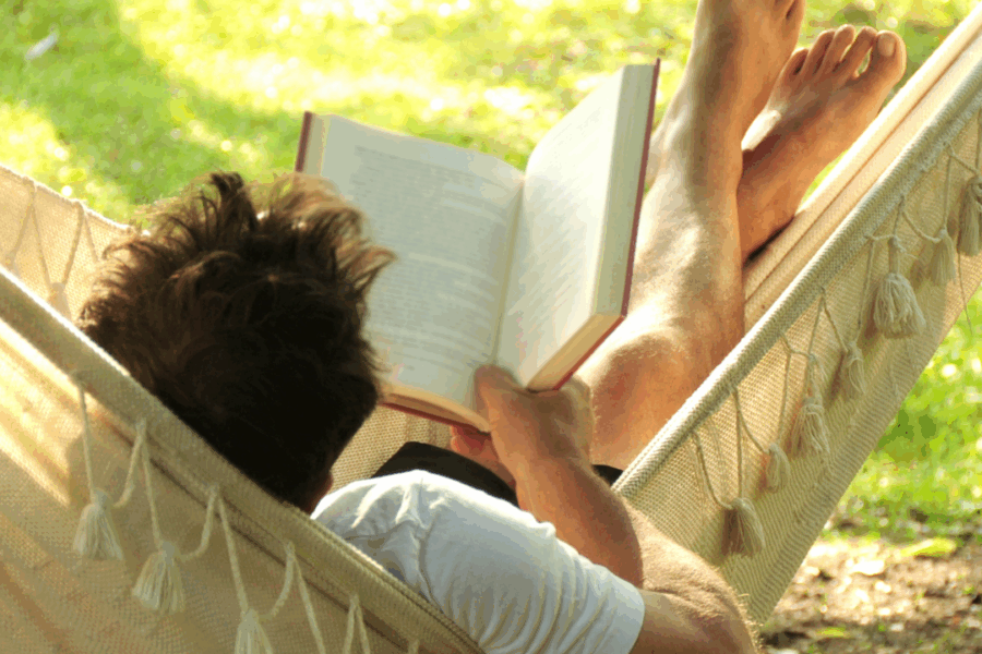 man getting some rest while relaxing on a hammock reading a book on a sunny summer afternoon